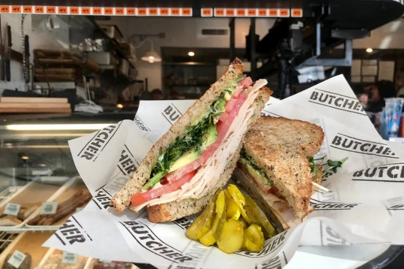 At a place whose name literally means "pig butcher," it’s easy to overlook a turkey sandwich. But at Donald Link’s Old World butcher and charcuterie shop, Cochon Butcher, that would be a mistake. It’s not just on the menu for folks who don’t eat pork. “With all the hearty sandwiches on the menu, we wanted to showcase a lighter, brighter sandwich but still have it carry a good depth of flavor,” says Link. That flavor comes from smoking giant turkey breasts in-house and layering slices of them on locally made seed bread with avocado, tomato, and fresh local sprouts with a vibrant basil aioli.