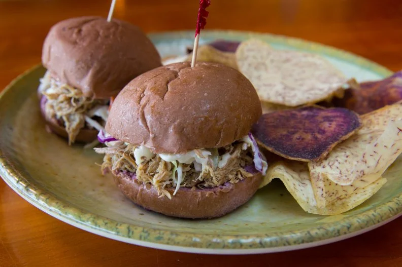 Kalua Pig is an age-old Hawaii specialty featuring meat cooked in an underground pit (known as an imu) with layers of wood, volcanic rock, banana trees and ti leaves, which imbue it with a soft earthy flavor. After steaming for six to 12 hours, kalua pork comes out tender and smoky — the perfect filling for a decadent sandwich. Versions can be found throughout the state, but the kalua pork sliders at Hawaii Inn are superb. Pork is prepared and hand-shredded according to a 70-year-old family recipe, nestled with bell peppers, onions and a hot Hawaiian chile aioli on a taro roll and served with colorful taro chips and salsa on the side.