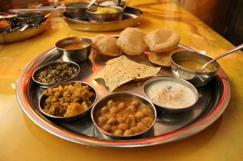 You won't need to queue up at steam tables for the limitless feast at Vatan, which specializes in the exclusively vegetarian cuisine of Gujarat, India. And you'll probably barely register that you're in Manhattan as you recline in a private booth capped with its own thatched roof while servers shuttle over appetizers, entrees and dessert. You can request seconds, thirds, fourths or more of everything â  as who can resist extra helpings of fried hot peppers with garam masala, red gravy-sauced potatoes over rice and pea pulao, and the rose syrup-sweetened waffle balls known as gulab jamun?