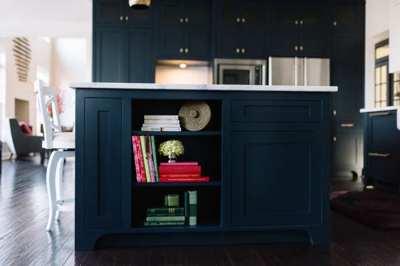 This striking kitchen remodel in navy blue and white, features a work island with marble countertop and storage.