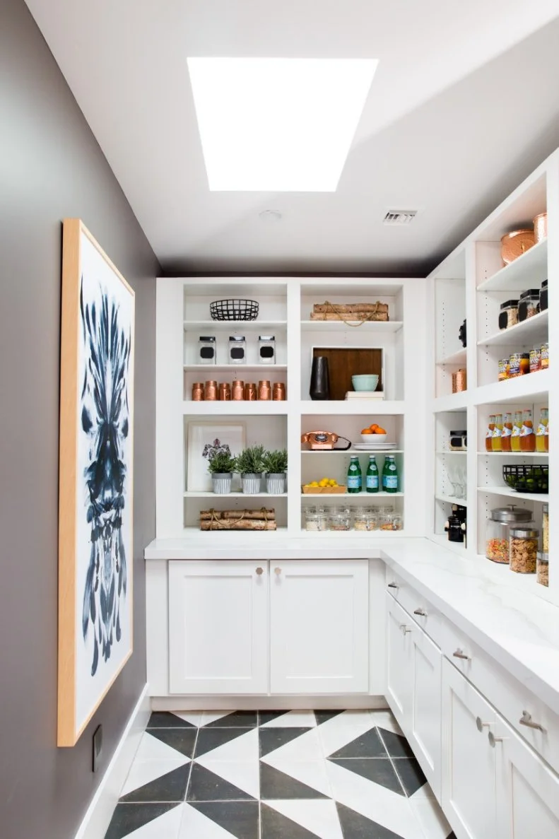 The storage area of the well-organized pantry also features quartz counters and Shaker-style white painted maple cabinet doors with wall art for decoration and the same funky hardware used for the black cabinets in the kitchen.