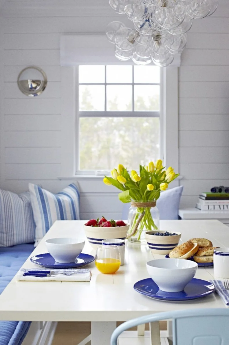Yellow tulips center the table to bring some cheer to the breakfast room. A cushioned, built-in banquette complements the blue and white dishware and creates an inviting place to enjoy a meal.