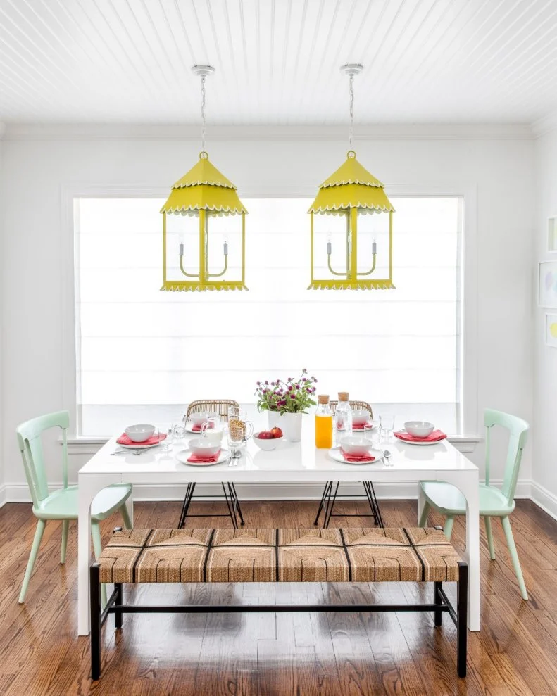 The casual nature of this breakfast nook is amplified by the mismatched seating arranged around a simple white dining table. To up the fun factor, the Chango & Co. design team added bright, yellow lantern-style pendant lights that work with the mint-colored chairs and watermelon pink table settings for a summery color scheme.