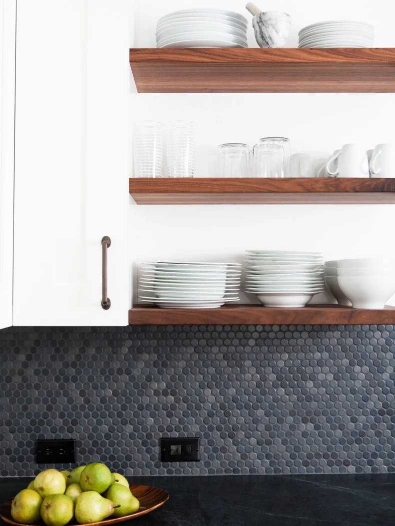 Open shelving is an attractive storage solution in this industrial-meets-modern kitchen. Gray penny tile on the backsplash blends neatly with the dark marble countertops, while clean white cabinetry keeps the space airy and bright.