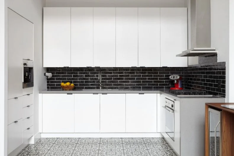 For this urban, modern kitchen, the black tile backsplash and patterned gray and white floor jazz up the basic white cabinets.