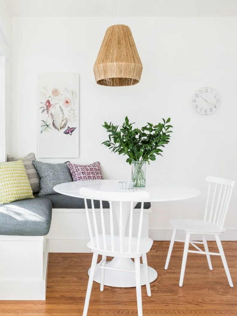 This breakfast nook is a perfect example of how the home's designers used a white base to layer on colors, patterns and textures and created a kid-friendly, so-stylish look. Graphic pillows visually pop off the gray bench cushion and a textured pendant complements the hardwood floor.