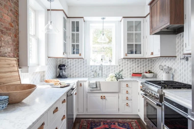The kitchen is a true gem with a patterned marble backsplash against exposed brick walls, a custom walnut range hood and walnut-trimmed white cabinety. Raw leather drawer and cabinet pulls add tactile appeal to the room.
