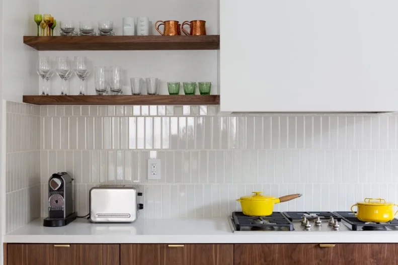 Rectangular tiles for the backsplash are laid vertically, creating height between countertops and open shelves. Warm woods contrast against the bright white walls and backsplash for a Scandinavian-inspired kitchen. 