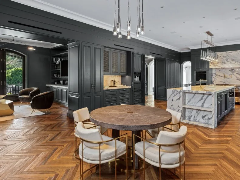 Matte black walls and a marble backsplash make a chic combination in this open-concept kitchen. In addition to custom cabinets and a large island, the space comes with a cozy dining space for breakfast.