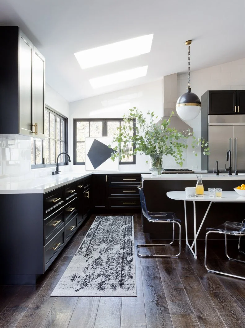 This transitional kitchen has two skylights for added natural light. It features an oversize island and black IKEA cabinets stretching from the rustic hardware floor up to the ceiling. Two globe pendant lights provide illumination for the space.