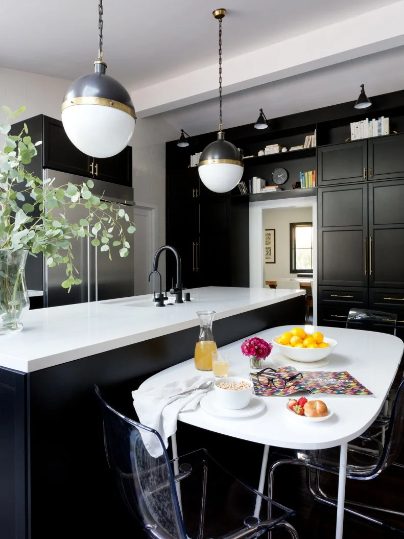 This transitional kitchen is part of a renovated 1960s home. It was moved to the back of the house and opened up with the removal of several walls. It features an oversize island and black floor-to-ceiling Ikea cabinets with Caesarstone countertops and high-end brass hardware. Two globe pendant lights provide illumination for the space.