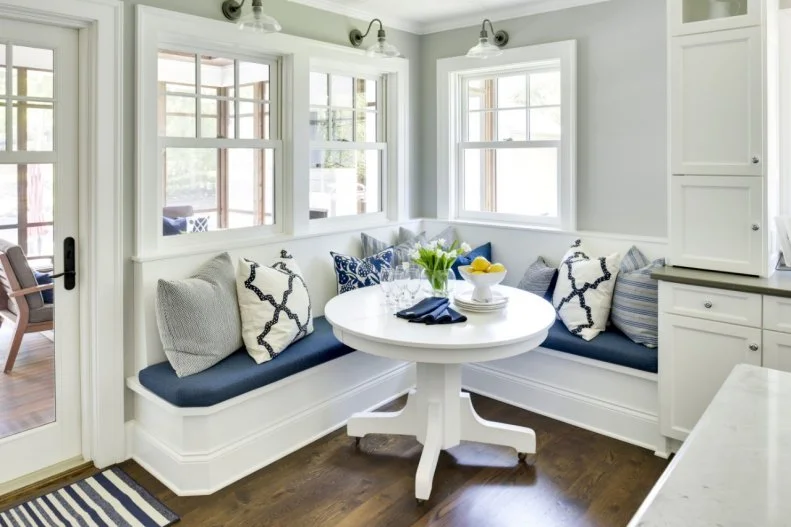 The pale gray walls of this lake home's breakfast nook are complemented by white furnishings, including an heirloom dining table, and accents of deep blue.