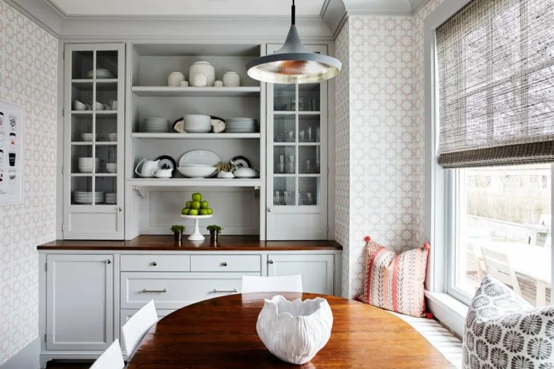 Located just off the kitchen, this breakfast nook comes with a built-in banquette, bright white chairs and a wooden table. Wallpaper with a gold pattern reflects the natural light and furthers the cheerful design.