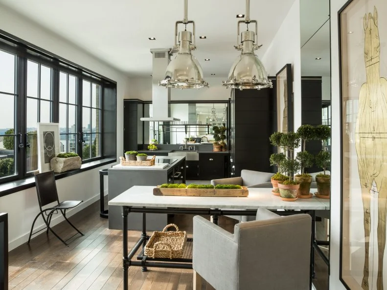 Topiaries and planters with moss bring life and a hint of lush greenery into this chic black and white kitchen. A long stretch of windows offers up breathtaking views to chefs and diners.