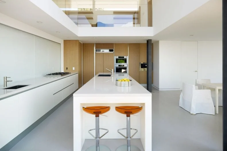 Sleek and sophisticated, this white, modern kitchen is perfectly uncluttered and large -- ready for cooking and guests. The island doubles as a breakfast bar; the bar stools add the room's pop of color. 