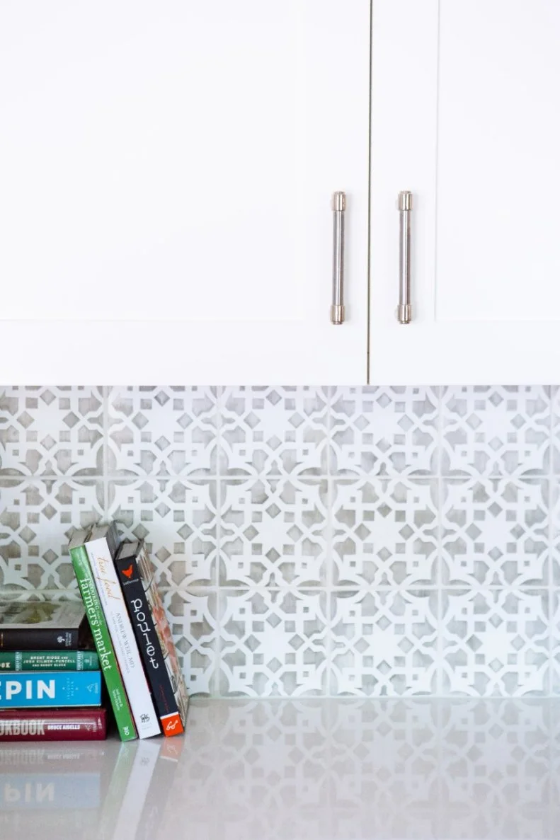 A graphic gray and white tile backsplash is the perfect complement for the crisp white cabinets and solid white countertops in this updated kitchen by Pure Design Interiors.
