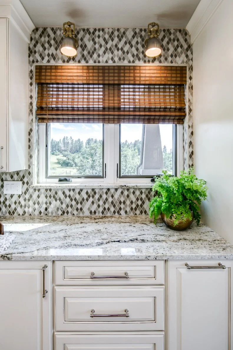 A mosaic tile backsplash featuring black, white and gray diamond-shaped tiles packs a powerful punch in this transitional kitchen. The backsplash — along with the graceful granite countertops — creates movement and visual interest against the creamy white cabinets.