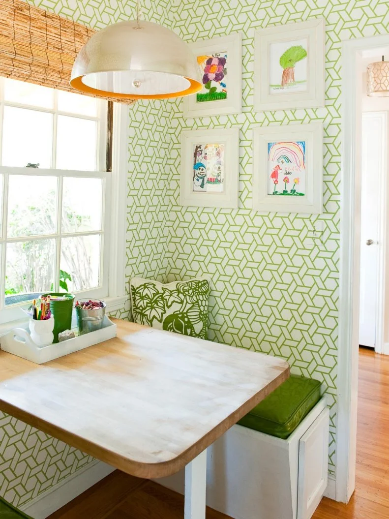 The playful basket-weave, green-and-white wallpaper makes a great background for the display of kids’ artwork.  Green cushions line the banquette seating, a retro pendant lamp illuminates the wood tabletop, and a bamboo blind sits atop the window. 