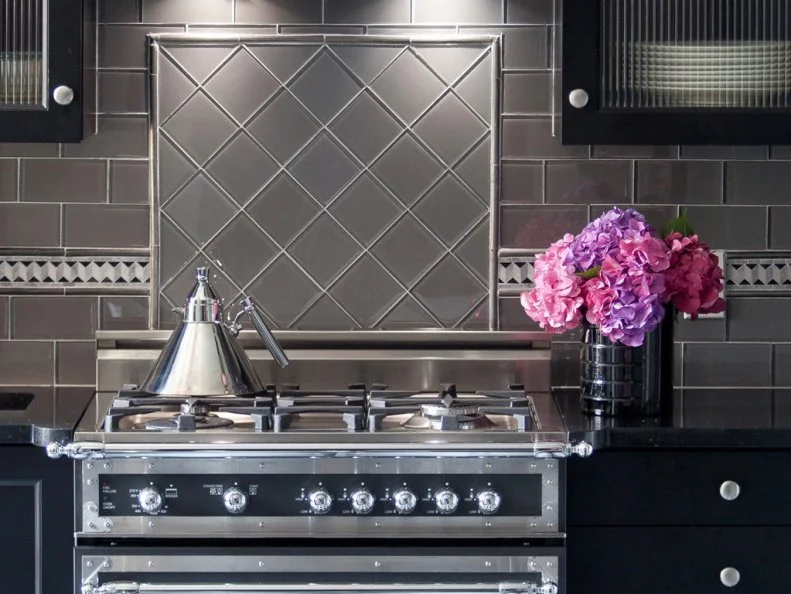 Clean lines on the stove range and walls give this art deco kitchen a layered feel. Stainless steel appliances tie together the gray tile. 