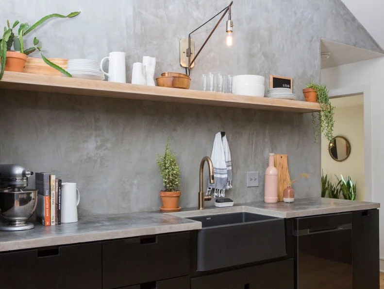 Black lower cabinets, with clean lines and no exterior hardware, along with gray concrete countertops, provide a strong base and visual contrast with the wood floors and open shelving in a light finish.