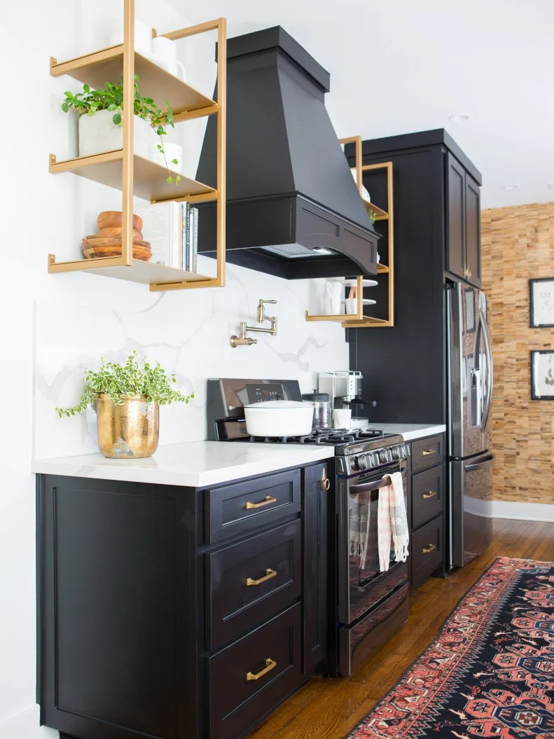 The redesigned kitchen blends the warmth of hardwood floors with the sharp contrast of the black cabinetry and white granite countertops. The distinctive wood wallpaper has gold flecks that create a subtle tie-in with the brass shelving and kitchen hardware.