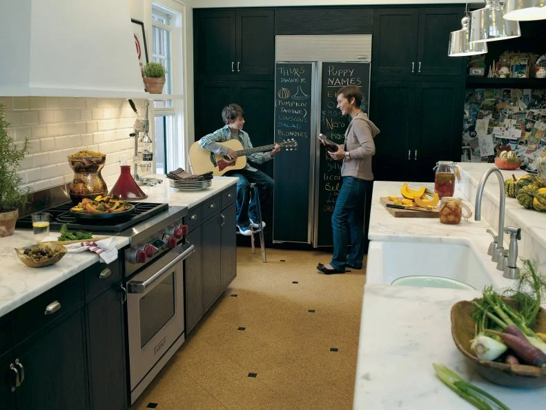 This narrow but smartly designed galley kitchen features black cabinets with marble countertops, a painted white brick backsplash and a refrigerator finished with chalkboard paint.