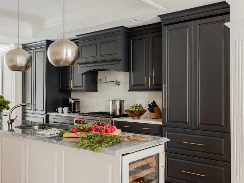 Black cabinets and drawers make a striking contrast against the white walls and kitchen island. Classic architectural details, like elegant columns and crown molding, combine with contemporary elements, such as the bubble pendant lights, to create a transitional chef's kitchen that is truly the heart of the home.