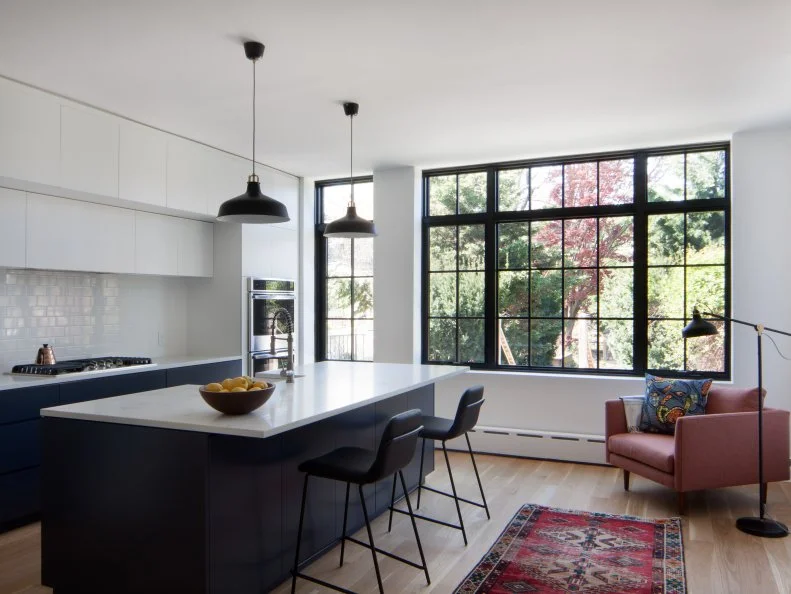 A richly colored Oriental rug and a simple armchair-plus-floor lamp reading nook cozies up the streamlined design of this modern kitchen.