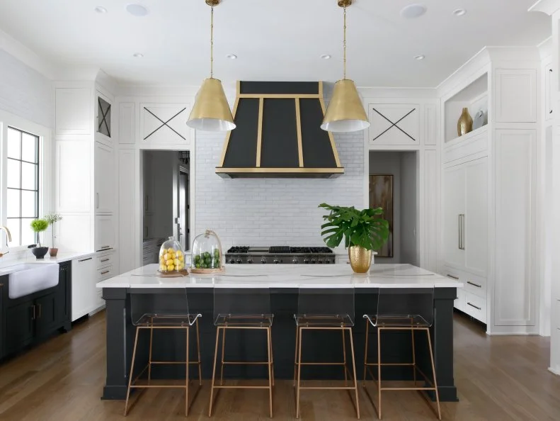 A single bank of black cabinets is a striking visual surprise in the kitchen, tying in with the same-colored island and range hood. Throughout the room, golden accents bring welcome warmth and glow.