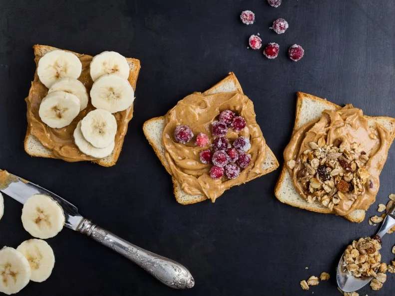 Peanut butter sandwiches with banana, candied cranberries  and healthy granola on gray background viewed from above
