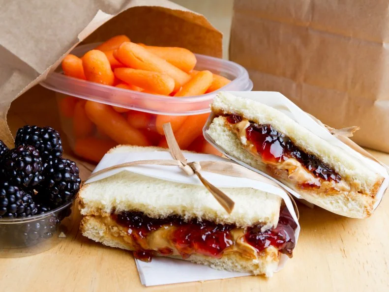Peanut Butter and Jelly sandwich with blackberries and carrots.  Brown bag lunch.