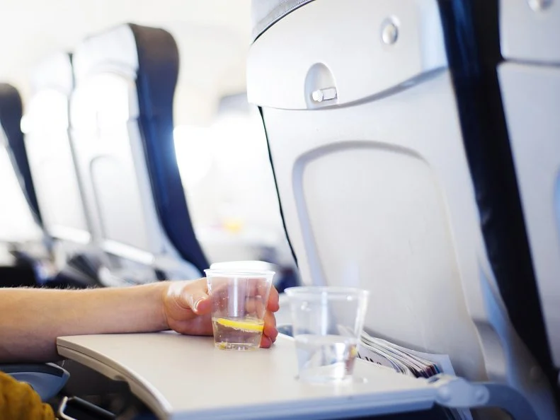 Happy man seating in the aircraft and drinking water before his trip abroad.