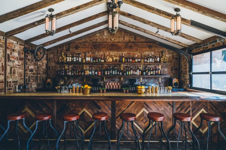 There’s a blend of Southwestern rusticity and Art Deco flare at the Urban Cowboy Public House, an indoor/outdoor bar set beside a smartly designed bed and breakfast. The bar itself, made from repurposed wood, is set in an old brick stable with exposed beams and dried herbs hanging overhead. Order food and drinks at the bar (go for the Rose Paloma for a grapefruit-spiked refresher) and then grab a seat inside at a communal table; outside by the fireplace; or near the smoky, wood-fired grill that acts as the bar’s rustic kitchen and pumps out wood-fired sausages and other snacks.
