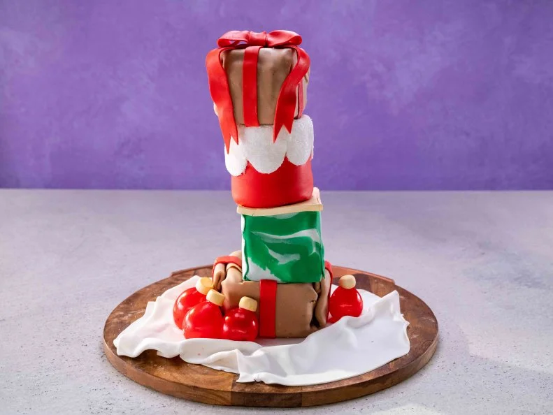 Contestant Nicholas Gomez's dish is Christmas Presents, with conquito cupcake with a cinnamon buttercream frosting (green box and top box), and Mexican hot chocolate with a marshmallow buttercream frosting (bottom box and red cylinder), during the final challenge, as seen on Cupcake Championship, Season 1.