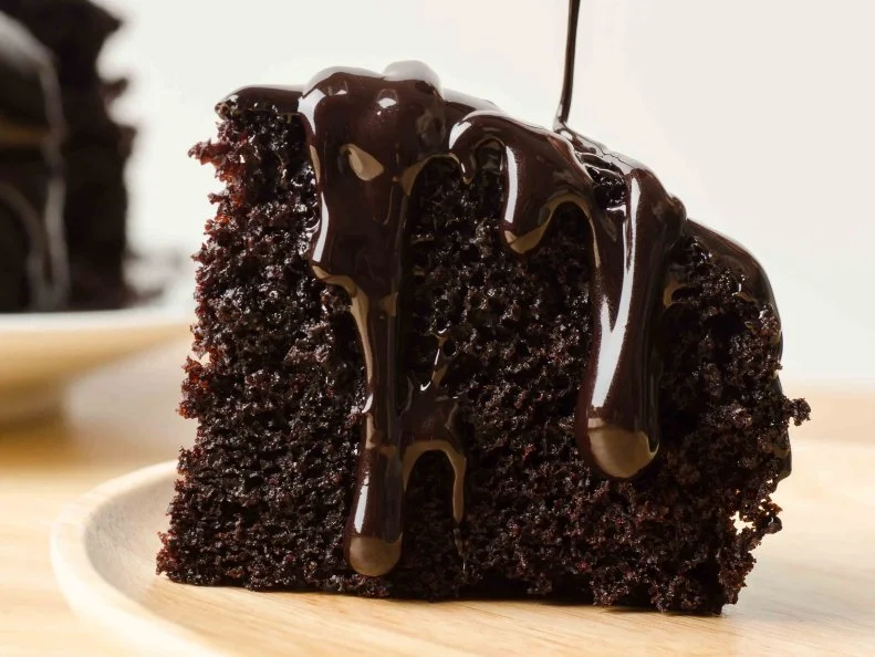 Pouring chocolate sauce on piece of chocolate cake