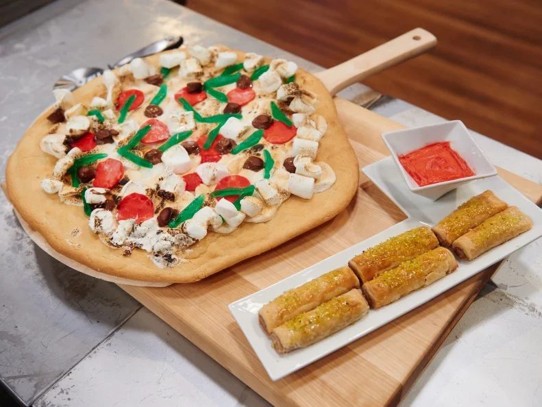 Contestant Payton Pelaez's dishes "Pizza with a sugar cookie crust with toasted marshmallow cheese, fondant pepperoni, gummy fish green peppers, and chocolate peanut butter olives, and Cinnamon Pie Dough 'Breadsticks' with Frosting" for the challenge "Dessert Imposters" as seen on Food Network's Kids Baking Championship, Season 1.