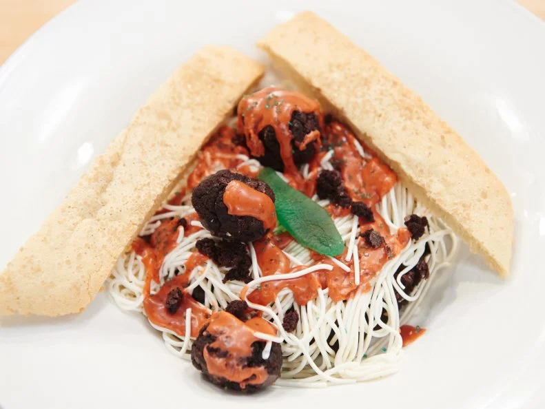 Contestant Cody Vasquez's dish "Spaghetti with Meatballs featuring Fondant-based spaghetti, brownie meatballs, red donut glaze, topped with a green sugar parsley with Toasted Biscotti 'Bread'" for the challenge "Dessert Imposters" as seen on Food Network's Kids Baking Championship, Season 1.