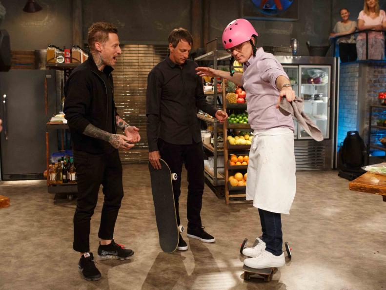 Co-Hosts Michael Voltaggio and Tony Hawk watch chef Bobby Flay ride his skateboard, as seen on Beat Bobby Flay, Season 20.