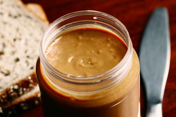 An open jar of crunchy peanut butter with bread and a knife.