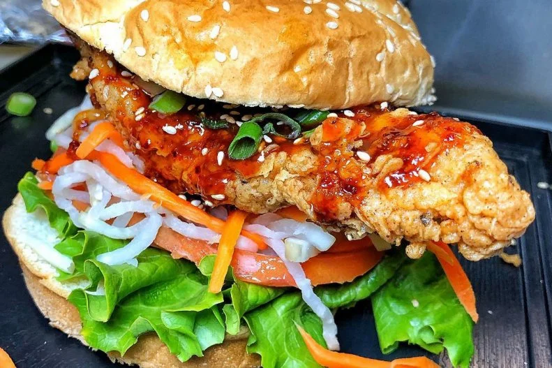 Combining owner Mi Sun Han’s Korean background with Executive Chef Boyzie Milner’s culinary know-how, the pair have raised the fried chicken sandwich to new international heights. At Buldogis Gourmet Hot Dogs, fresh chicken breasts are marinated overnight in a mix of soy sauce, sea salt and garlic brine to make them tender and infuse them with savory flavors. Each one is double-breaded in seasoned flour and deep-fried until golden brown. It's cradled in a sesame kaiser bun with crisp romaine lettuce, sliced beefsteak tomatoes and refreshing banh mi slaw, and finally drizzled with a tangy and bold Korean gochujang sauce.