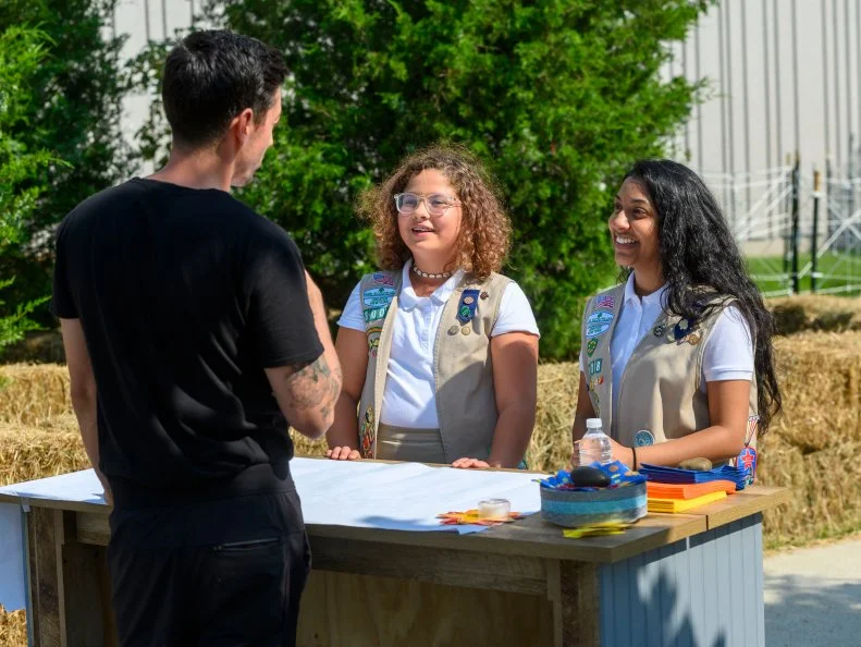 Girl Scouts Alyssa Dass and Victoria Gorain help competitor Eric See prepare his booth for the space inspired cookie pops tasting and judging, as seen on Girl Scout Cookie Championship, Season 1.