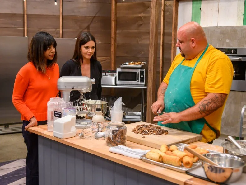 Judges Katie Lee and Samantha Seneviratne check in on competitor Vincenzo Vaccaro as he races to finish his s’mores inspired dessert, as seen on Girl Scout Cookie Championship, Season 1.