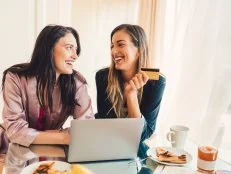 Happy sisters eating breakfast and shopping online with credit card   ++++ Note for the inspector: Credit card is fake ++++