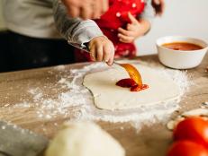 child preparing pizza with parent