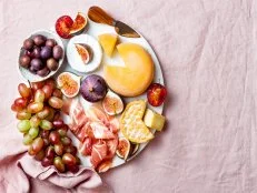 Appetizers, antipasti snacks. Cheese and fruit platter on marble board over pink linen tablecloth background. Top view, copy space