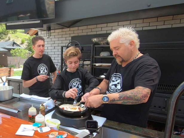 Host Guy Fieri and his Sons Hunter Fieri and Ryder Fieri Tasing a Sent Dish in the outdoor kitchen at Guy's House in Santa Rosa, California as seen on Food Network's Diners, Drive-Ins and Dives: Take Out episode DV3203H.