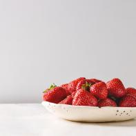 Fresh organic garden strawberries in ceramic plate on white marble table. Copy space.