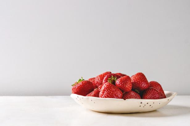 Fresh organic garden strawberries in ceramic plate on white marble table. Copy space.