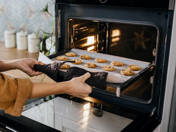 Young mother is putting a tray full of cookies which they made together with her husband and her son in the oven. Horizontal photo. Face is not visible.