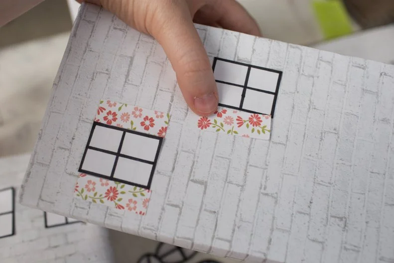 Using your glue stick, glue the windows, doors, and shutters on each of the boxes wherever you think they’ll look best. Get creative! 